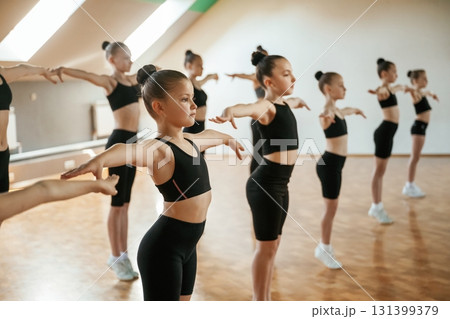 Standing together. Group of female kids practicing athletic exercises indoors Standing together. Group of female kids practicing athletic exercises indoors 131399379
