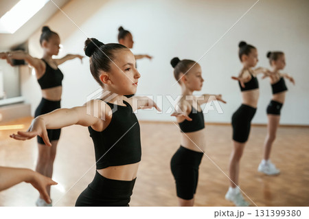 Standing together. Group of female kids practicing athletic exercises indoors Standing together. Group of female kids practicing athletic exercises indoors 131399380