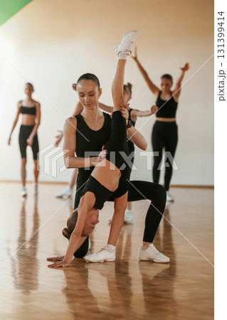 Trainer is helping girl. Group of female kids practicing athletic exercises together indoors 131399414