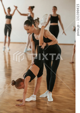 Trainer is helping girl. Group of female kids practicing athletic exercises together indoors 131399415