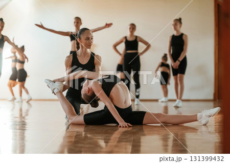 Process of helping the girl by coach. Group of female kids practicing athletic exercises together indoors Process of helping the girl by coach. Group of female kids practicing athletic exercises together indoors 131399432