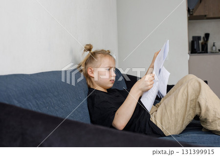 Serious little girl sitting on sofa reading book at home. Childhood and people concept Serious little girl sitting on sofa reading book at home. Childhood and people concept 131399915
