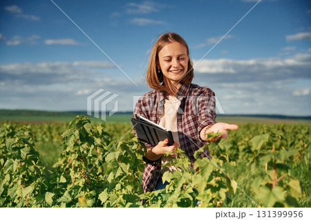 Digital tablet in hands. Young woman is on the beautiful agricultural field at daytime Digital tablet in hands. Young woman is on the beautiful agricultural field at daytime 131399956