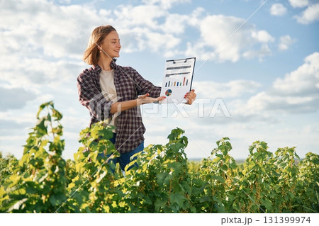 Important data in document. Young woman is on the beautiful agricultural field at daytime 131399974