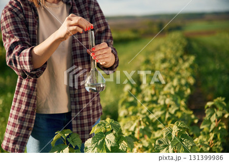With test tube, doing research. Young woman is on the beautiful agricultural field at daytime With test tube, doing research. Young woman is on the beautiful agricultural field at daytime 131399986