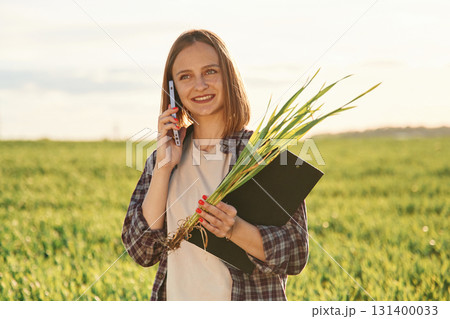 Using smartphone. Young woman is on the beautiful agricultural field at daytime Using smartphone. Young woman is on the beautiful agricultural field at daytime 131400033