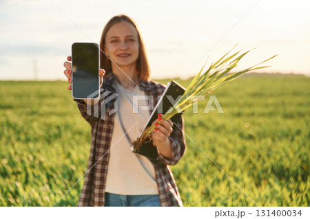 Using smartphone. Young woman is on the beautiful agricultural field at daytime 131400034
