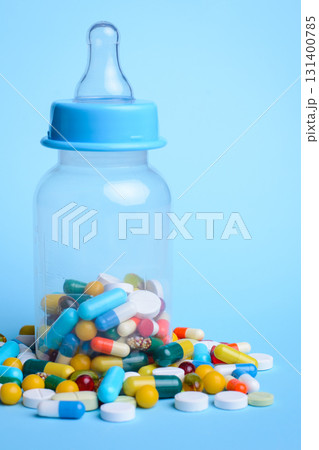 Concept of baby taking pills. Baby`s milk bottle full of pills and capsules against the blue background 131400785