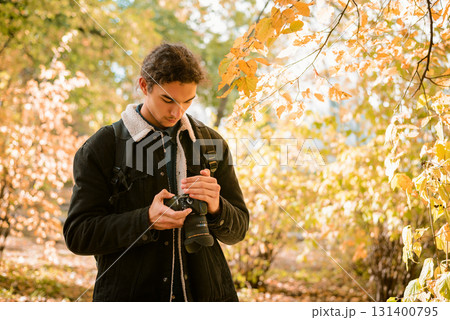 Landscape and nature photographer looking through his shots on camera, standing in forest between yellow, red autumn trees 131400795