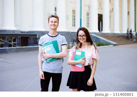 Two happy students in front of university with books and exercise books Two happy students in front of university with books and exercise books 131400801