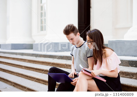 Male and female teenage friends using computer sitting on stairs of university or college working on project 131400809