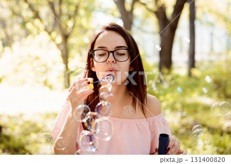 Attractive female girl blowing soap bubbles in the park, having good time and enjoying her free time Attractive female girl blowing soap bubbles in the park, having good time and enjoying her free time 131400820