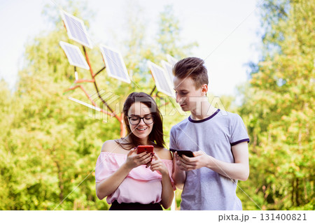 Male and female students against solar panels, using advantages of renewable energy, using modern devices that were charged with a help of street solar station 131400821