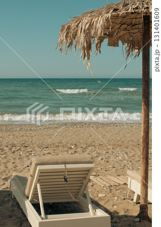 Simple beach scene on Crete - sunbeds and palm leaf umbrellas by the pebbles and sea Simple beach scene on Crete - sunbeds and palm leaf umbrellas by the pebbles and sea 131401609