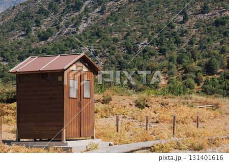 Wooden brown outdoor toilet cabin at the foot of mountains on sunny summer day Wooden brown outdoor toilet cabin at the foot of mountains on sunny summer day 131401616