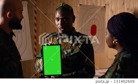 Soldiers at shooting range do training designed to increase safety and survivability in combat, watching instructional videos on green screen chroma key tablet device presented by commander, camera B Soldiers at shooting range do training designed to increase safety and survivability in combat, watching instructional videos on green screen chroma key tablet device presented by commander, camera B 131402609