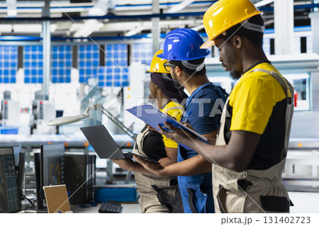 African american workers checking up on manufacturing equipment in solar panel factory, reading documentation files. Team of engineers in industrial facility inspecting production process. 131402723