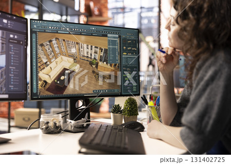 Young designer works on remodeling project using architectural software on PC to configure room layouts. The program allows her to drag and drop elements or assets, adjusting virtual furniture. 131402725