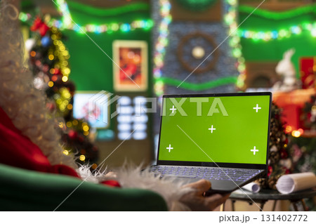 Close up of Santa Claus using mockup laptop to arrange delivery routes for Christmas Eve. Santa plots winter holidays event journey to children houses using isolated screen notebook Close up of Santa Claus using mockup laptop to arrange delivery routes for Christmas Eve. Santa plots winter holidays event journey to children houses using isolated screen notebook 131402772