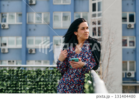Businesswoman in Black Suit Using Smartphone on Break in Modern Urban Environment. 131404480