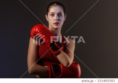Confident young female boxer with red gloves posing in studio, athletic strength, focus and fitness training Confident young female boxer with red gloves posing in studio, athletic strength, focus and fitness training 131405501
