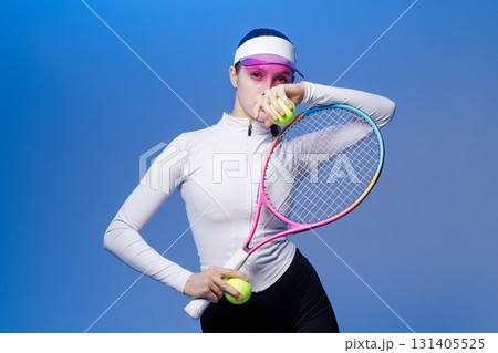 Confident tennis player holds racket and balls in studio on blue background, ready for training and competition Confident tennis player holds racket and balls in studio on blue background, ready for training and competition 131405525