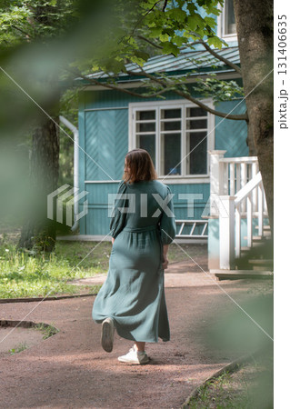 A woman in a flowing green dress spins gracefully on a garden path in front of a wooden house A woman in a flowing green dress spins gracefully on a garden path in front of a wooden house 131406635