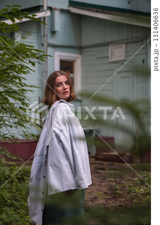 A close-up portrait of a woman in a green dress with a denim jacket draped over her shoulders standing near a pastel-colored wooden house A close-up portrait of a woman in a green dress with a denim jacket draped over her shoulders standing near a pastel-colored wooden house 131406636