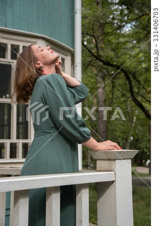 A woman in a green dress leans on a white wooden railing in front of a turquoise house, smiling at the camera 131406703