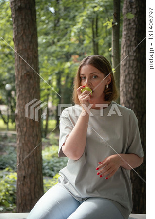 Woman in a light grey T-shirt eats a green apple in a forest park in Peredelkino, Russia Woman in a light grey T-shirt eats a green apple in a forest park in Peredelkino, Russia 131406797