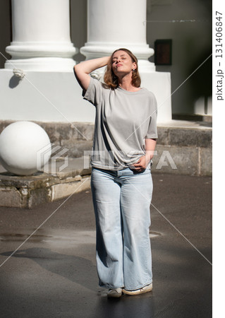Young woman in light jeans and gray t-shirt standing under the sun in front of classical white columns, enjoying a peaceful moment Young woman in light jeans and gray t-shirt standing under the sun in front of classical white columns, enjoying a peaceful moment 131406847