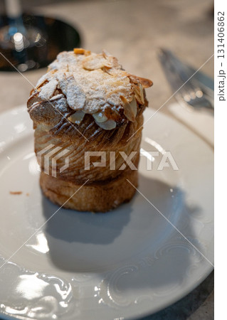 Golden almond cruffin topped with powdered sugar and sliced almonds, served on an elegant white plate 131406862