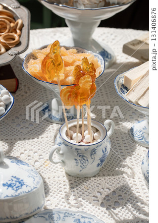 Traditional Russian sweets including rooster lollipops, baranki, zephyr, and candied fruits served in vintage porcelain and silverware under sunlight 131406876