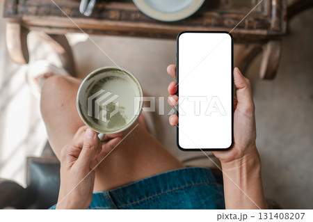 Overhead view of a woman holding a coffee cup and smartphone with a blank screen, ideal for mockups or design presentations. 131408207