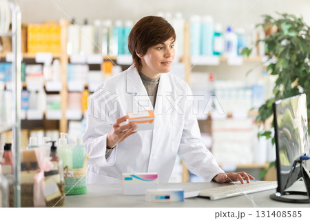 Female pharmacist checking stock of medicines, offering to customer at pharmacy Female pharmacist checking stock of medicines, offering to customer at pharmacy 131408585