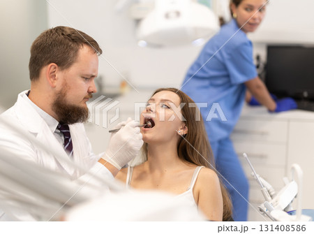 Male doctor checks young woman teeth during visit to dental clinic Male doctor checks young woman teeth during visit to dental clinic 131408586