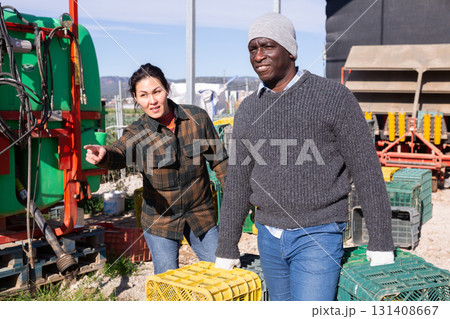 Female farmer giving instructions to worker carrying plastic crates 131408667
