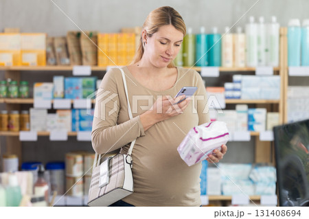 Pregnant woman scanning barcode on feminine pads in drugstore 131408694