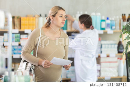 Pregnant woman with prescription looking for items in pharmacy 131408713
