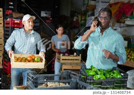 Owner of vegetable warehouse is talking on mobile phone while other workers are sorting vegetables 131408734