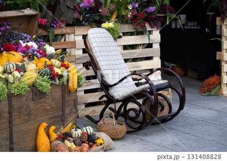 Autumnal scene with a rocking chair, gourds, and flowers in a rustic setting. 131408828