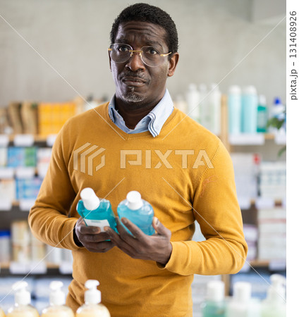 In sales area of pharmacy, African man examines packaging of mouthwash In sales area of pharmacy, African man examines packaging of mouthwash 131408926