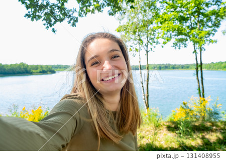 A Smiling Young Woman Enjoying Time by a Serene Lake Surrounded by Lush Greenery A Smiling Young Woman Enjoying Time by a Serene Lake Surrounded by Lush Greenery 131408955