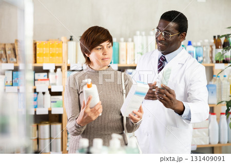 Woman choose buy emollient cream at pharmacy. African man in background 131409091