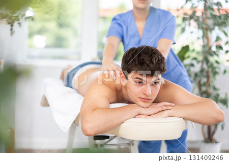 Masseuse doing back massage to young guy Masseuse doing back massage to young guy 131409246