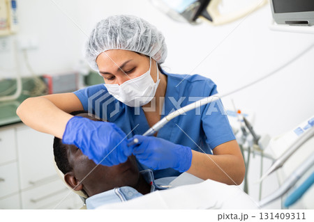 Female dentist using tools for tooth repairing on man patient 131409311
