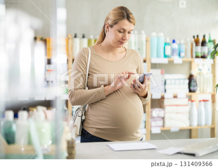 Young woman scrolling phone while looking for something in drugstore Young woman scrolling phone while looking for something in drugstore 131409366