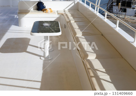 Sunny yacht deck with white seating and table overlooking marina Sunny yacht deck with white seating and table overlooking marina 131409660