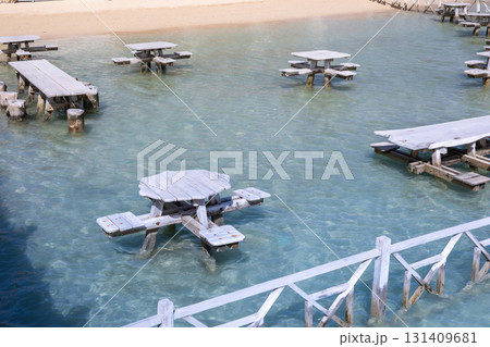 Unique outdoor seating area with wooden picnic tables above clear water by sandy beach 131409681