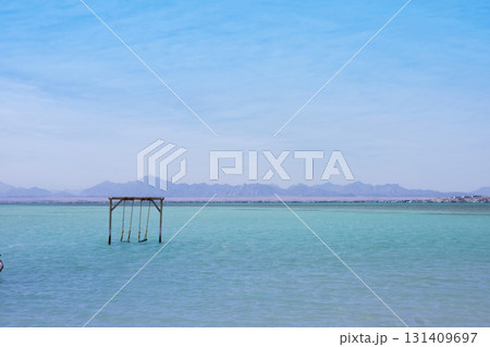 Tranquil seaside scene with wooden swing set against distant mountains Tranquil seaside scene with wooden swing set against distant mountains 131409697